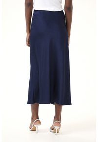 Jupe en satin bleu marine au design fluide, coupée mi-longue et avec une texture subtile. Associée à des sandales à talons hauts argentées.