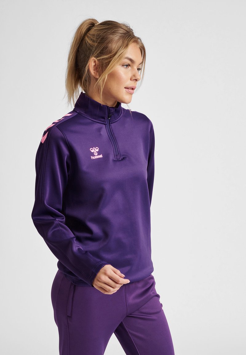 Haut de sport zippé violet avec col haut, manches longues et accents de logo rose. Fabriqué en matériau synthétique lisse adapté aux vêtements d'activités.