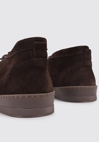 Botas de tobillo de ante marrón con una superficie texturizada, punta redondeada y suela de goma. Presentan un tacón bajo y un detalle de costura mínima.