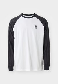 Majica z dolgimi rokavi z belo podobo in črnimi črtastimi raglan rokavi. Ima črn logotipni pečat na prsih in enobarvne črne manšete.