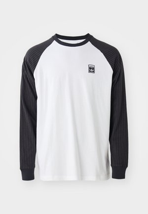Majica z dolgimi rokavi z belo podobo in črnimi črtastimi raglan rokavi. Ima črn logotipni pečat na prsih in enobarvne črne manšete.