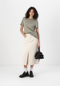 Olive green cotton t-shirt, cream midi skirt with front slit, black chunky shoes, and a black floral-patterned handbag.