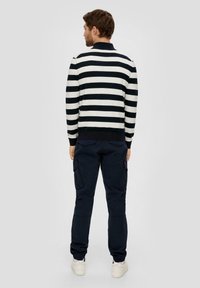 Striped knit sweater in black and white, paired with navy cargo pants, featuring side pockets and elastic cuffs, worn with white sneakers.