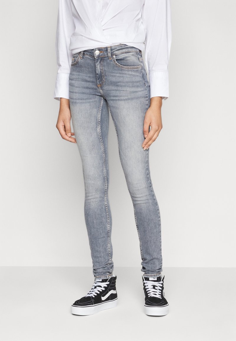 Vaqueros ajustados en denim de color azul claro, con un diseño clásico de cinco bolsillos y un ligero desvanecimiento. Combinados con zapatillas negras y una camisa blanca.
