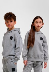 Grå huhoodtröjor av mjukt tyg med framficka och svart logotypmärke; kombinerade med matchande byxor för en samordnad look.