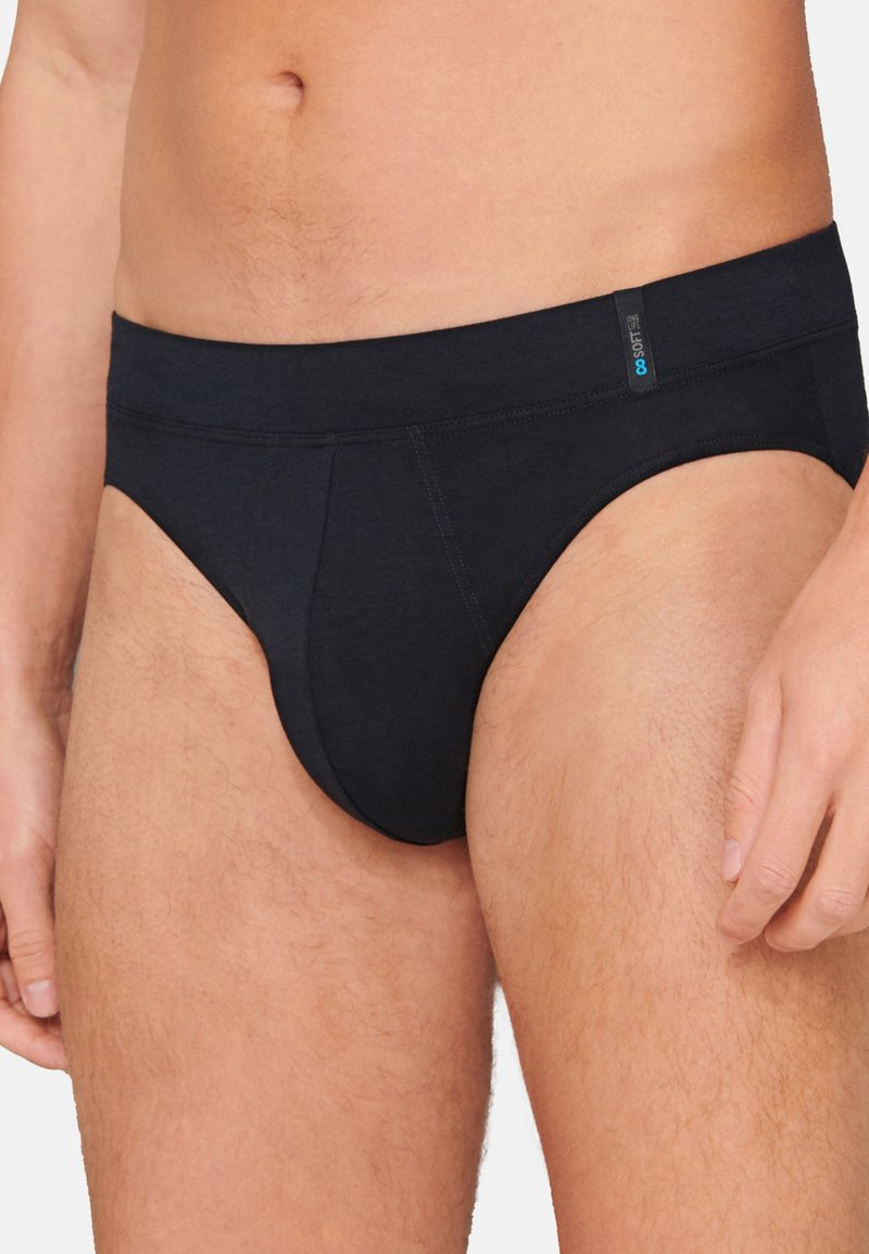 Tanga in cotone nero con una texture liscia, vita bassa e etichetta blu discreta sulla cintura. Vestibilità classica con dettagli di cucitura minimi.