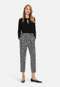 Schwarzes Langarmoberteil mit einem Schlüsselloch-Detail, kombiniert mit einer Hose im Leopardenmuster mit Taschen und schmal zulaufenden Beinen; schwarze Ballerinas runden den Look ab.