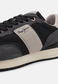 Mustvalge dressid, millel on seemis- ja võrkmaterjalid. Omab beeži külgpaneeli ja musta kummist tallatööd. Lukkudega disain koos logodetailiga.