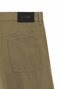 Pantaloni verde oliva con una texture liscia e opaca; presentano una tasca posteriore e un'etichetta in pelle nera embossata con la scritta "BOSS."
