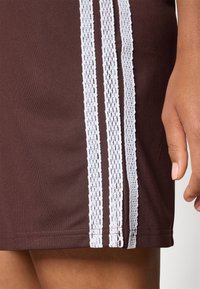 Brown athletic skirt featuring three vertical white stripes and a textured knit pattern along the sides, with a smooth, fitted fabric.