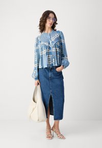 Blåmønstret bluse med plissee, parret med en denimnederdel med en foran slids. Hvid håndtaske og sandleder med remme fuldender looket.