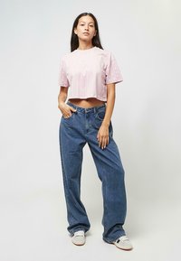Orezané ružové pásikavé tričko s krátkymi rukávmi v kombinácii s voľnými modrými džínsami. Oblečenie má ležérny dizajn, viditeľné stehy a textúru džínsoviny.