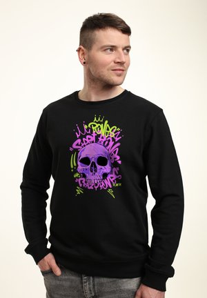 Zwarte sweatshirt met een kleurrijke schedelillustratie in paars en groen, met graffiti-stijl tekst en accenten, gemaakt van zachte stof.