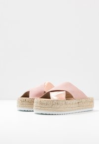 Růžové espadrilky s křížovým designem pásků. Mají jutovou podrážku, texturovanou látku a lesklý kovový akcent na svršku.