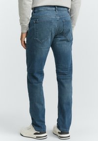 Denim jeans in medium blue met een rechte pijp, voorzien van twee achterzakken, subtiele vervagingen en een zachte textuur. Zwart-witte schoenen eronder.
