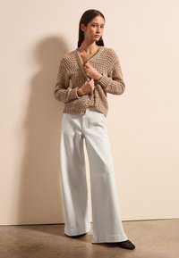 Cárdigan de punto beige con escote en V y botones frontales, combinado con pantalones de pierna ancha azul claro y zapatos negros texturizados.