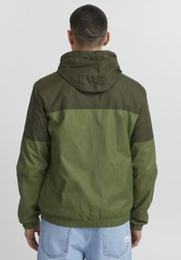 Green hooded jacket featuring a two-tone design with dark and light green sections, made from a lightweight, water-resistant material.