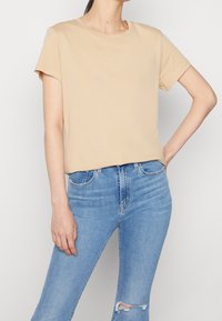 T-shirt beige en coton avec un col rond et des manches courtes, portée rentrée dans un jean skinny bleu délavé à taille haute.