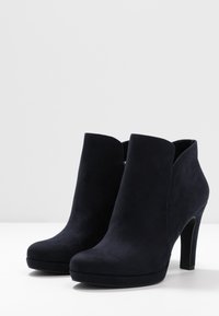 Černé semišové kotníkové boty s vysokým podpatkem, kulatou špičkou a vyříznutými boky. Hladký povrch a minimalistický design, vhodné pro formální nošení.