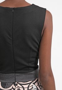 Zwarte mouwloze top met een gladde afwerking, voorzien van een korte rits aan de achterkant en een grijze tailleband, gecombineerd met een gestreepte rok.