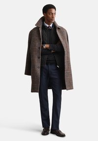 Barna kockás kabát fekete steppelt mellény fölött, sötétkék nadrággal és sötét cipővel. Magas gallérral és gombos elülső zárral rendelkezik.