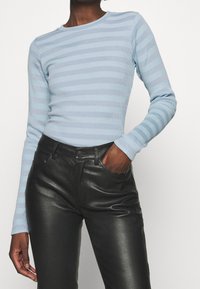 Hellblaues, geripptes Longsleeve-Oberteil mit abwechselnden hellen und dunklen Streifen, kombiniert mit schwarzen, hochgeschnittenen Lederhosen.
