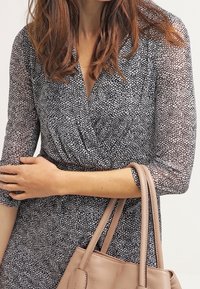 Svart och vit mönstrad omlotklänning med 3/4 ärmar, gjord av lätt tyg, i kombination med en beige handväska.