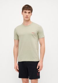 T-shirt en coton vert clair avec un col rond et des manches courtes, arborant un petit logo rouge "HUGO" sur la poitrine.