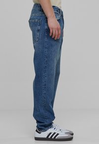 Lyseblå denimjeans med en afslappet pasform, fem-lomme design, synlig syning og kontrast hardware; parret med hvide og grå sneakers.