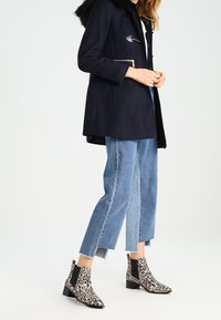 Marinblå ullkappa med fuskpälskrage och dragkedjedetaljer; kombinerad med korta jeans och svartvita ankelstövlar med leopardmönster.