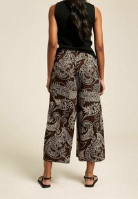 Pantalons larges marron avec un motif paisley blanc, en tissu léger, taille élastique et longueur cropped. Associés à un haut sans manches noir.