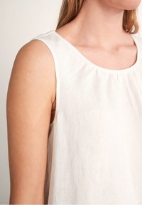 Weißes ärmelloses Top aus Leinen mit rundem Ausschnitt, dezentem Kräuseleffekt am Hals und einem lockeren Schnitt. Glatte Textur, schlichtes Design.