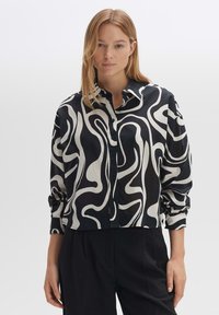 Camicia a maniche lunghe, sfitta, con bottoni, in bianco e nero con un motivo a linee ondulate. Realizzata in un tessuto liscio, presenta un colletto aperto e maniche con polsini.