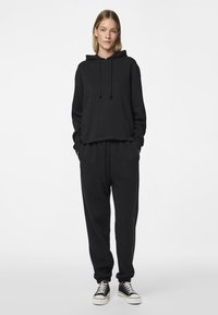 Μαύρο φούτερ με κουκούλα, κορδόνι, άνετη εφαρμογή και μακριά μανίκια, σετ με αντίστοιχο μαύρο παντελόνι φόρμας με ελαστική μέση και μανσέτες.