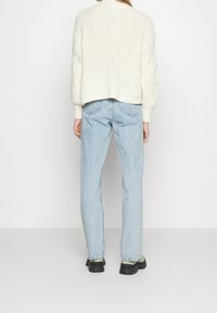 Cream chunky knit sweater with a high collar, paired with light blue straight-leg jeans and black rubber-soled boots.