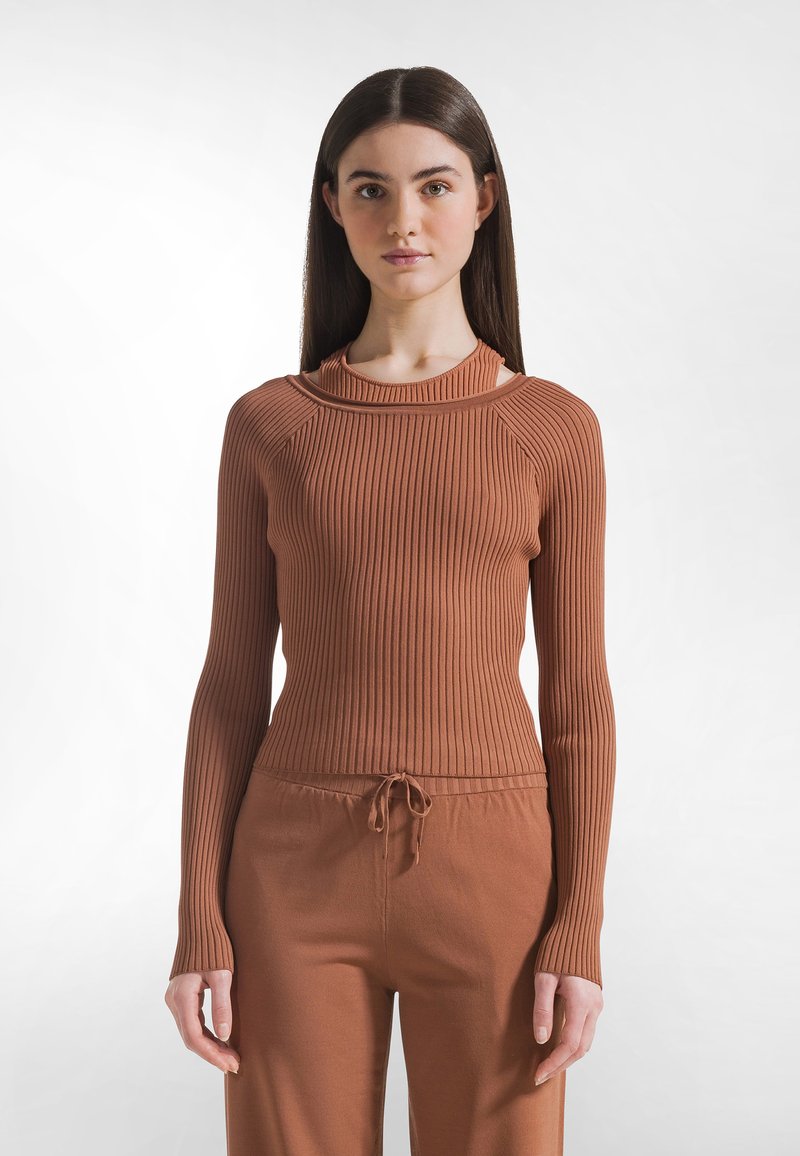 Top a maniche lunghe costellato color ruggine con collo alto, caratterizzato da tagli sulle spalle e design aderente, abbinato a pantaloni coordinati.