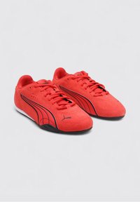 Baskets de sport en daim rouge avec des rayures et des accents noirs, dotées d'un système de laçage et d'une semelle blanche. Design classique avec une finition texturée.