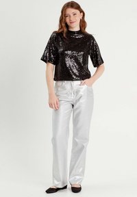 Top negro de lentejuelas de manga corta combinado con pantalones anchos plateados brillantes, que presentan un corte recto y una textura suave. Unos zapatos planos negros completan el look.