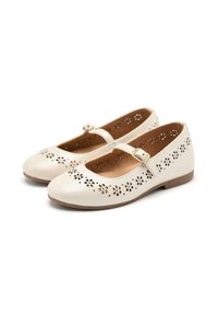 Zapatos Mary Jane color crema de cuero con patrones florales perforados, punteras redondeadas y una correa con un detalle de hebilla metálica.