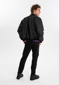 Black bomber jacket, textured fabric, ribbed cuffs and hem. Paired with black cargo pants featuring side pockets and black shoes.