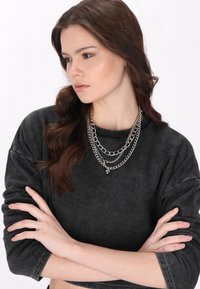 Felpa in denim nero con maniche lunghe, finitura testurizzata. Presenta collane a catena argentata sovrapposte con maglie di diverse dimensioni e un ciondolo a forma di cuore.