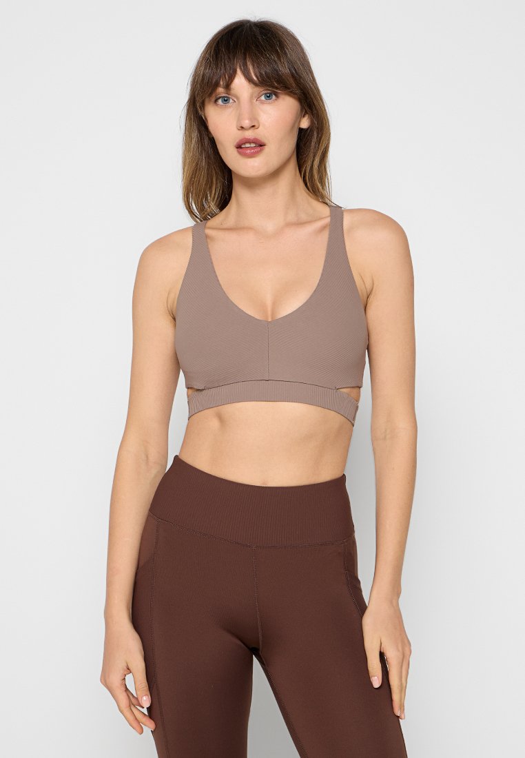 Sport-Bra aus hellbraunem Rippstoff mit tiefem V-Ausschnitt, breiten Trägern und einem Unterbrustband. Kombiniert mit hoch taillierten braunen Leggings.