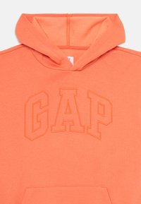 Hoodie arancione con un grande logo "GAP" ricamato. Il tessuto è morbido con una superficie liscia. Include un cappuccio con coulisse e una tasca frontale.