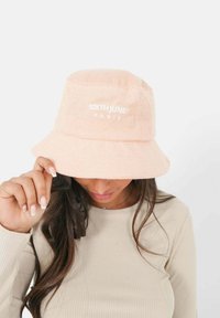 Perzikkleurige bucket hat van zacht badstof met geborduurd "SIXTH JUNE PARIS" logo in het wit. De rand is breed en gestructureerd.