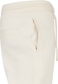 Pantalones de chándal color crema con un tejido texturizado, cinturilla elástica con cordón y un bolsillo lateral de diseño minimalista.