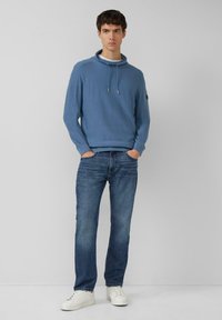 Jasnoniebieska bluza z kapturem, ze ściągaczami i ściągaczami przy mankietach, zestawiona z niebieskimi dżinsami i białymi trampkami. Prosty, casualowy design.