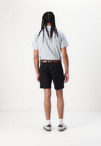 Chemise à manches courtes rayée avec un ourlet droit, shorts noirs, ceinture marron, chaussures noires à tige basse et chaussettes blanches, vue de dos.