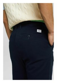 Námořnické modré kalhoty vyrobené z bavlněné směsi, obsahující zadní kapsu s knoflíkem a malou bílou nášivku s logem. Texturovaný svetr s kabelovým pletením nahoře.