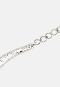 Chaîne en argent avec des maillons ovales reliés à un pendentif en métal incurvé et texturé sur un fond blanc.