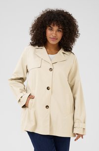 Beige, lichtgewicht jas met een kraag, vier knopen en twee zijzakken. Heeft een ontspannen pasvorm en zichtbare manchet-details.